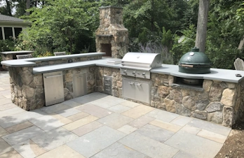 Cozy outdoor setup with a brick chimney, bar, and kitchen with a smoker in Concord, Massachusetts, perfect for gatherings and cooking