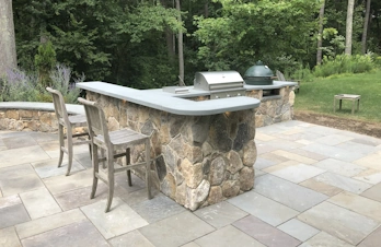 Rustic outdoor kitchen in Concord, Massachusetts, with a brick chimney, bar, and smoker, ideal for cooking and entertaining