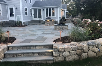 Raised patio with a fire pit, outdoor kitchen, and seating in Concord, Massachusetts